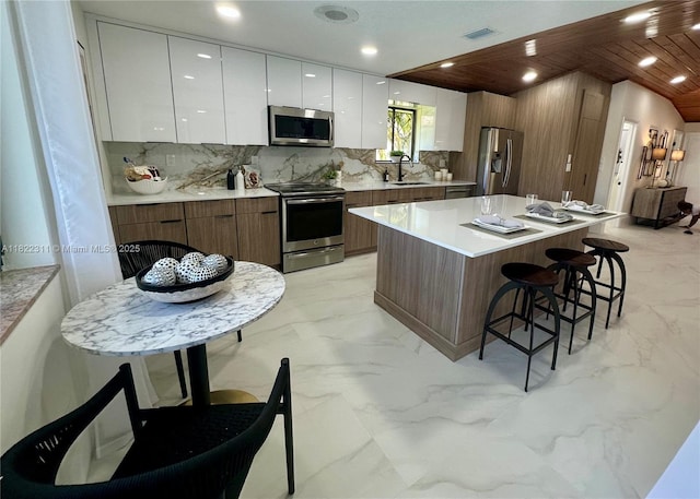 2019 NW 108th Ln, Coral Springs, FL 33071 - kitchen featuring stainless steel appliances, modern cabinets, light marble finish floors, a breakfast bar, and white cabinetry
