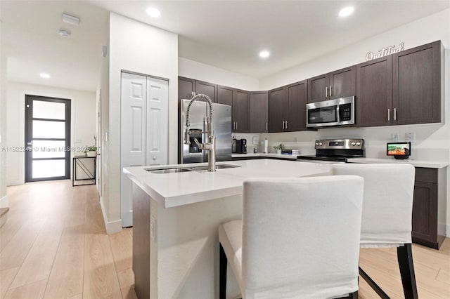 10129 W 32nd Ln, Hialeah, FL 33018 - kitchen featuring stainless steel appliances, a kitchen island with sink, dark brown cabinets, light wood-style floors, and recessed lighting