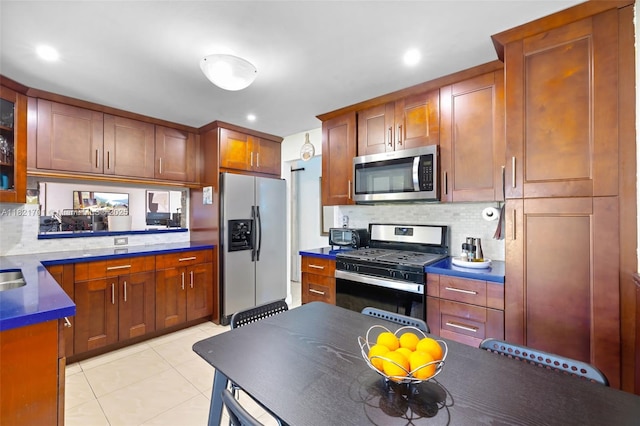 18401 SW 115th Ave, Miami, FL 33157 - kitchen with stainless steel appliances, decorative backsplash, light tile patterned floors, brown cabinetry, and glass insert cabinets