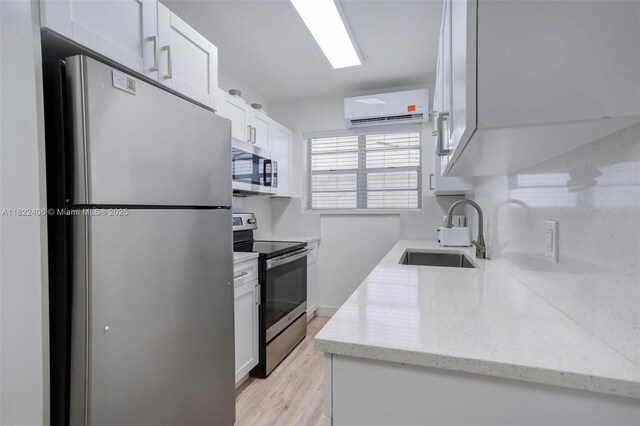4015 Indian Creek Dr Unit 106, Miami Beach, FL 33140 - kitchen featuring appliances with stainless steel finishes, an AC wall unit, white cabinets, light wood-type flooring, and light stone counters