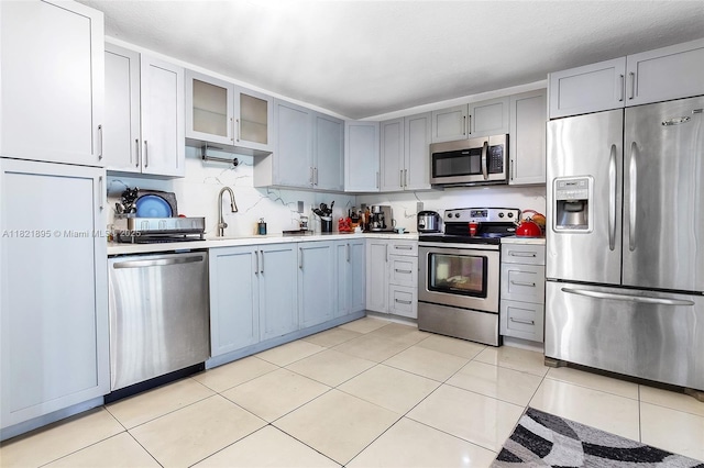 3430 NW 16th St, Miami, FL 33125 - kitchen featuring stainless steel appliances, light countertops, gray cabinets, light tile patterned floors, and glass insert cabinets