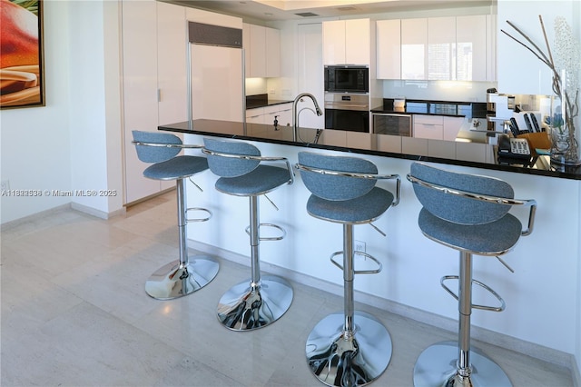 1425 Brickell Ave Unit 48C, Miami, FL 33131 - kitchen with built in appliances, dark countertops, white cabinets, and a kitchen bar