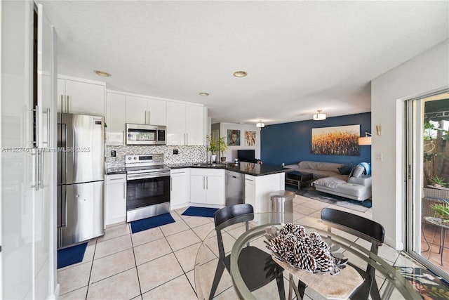 11018 NW 47th Ter, Doral, FL 33178 - kitchen with stainless steel appliances, dark countertops, a peninsula, white cabinets, and decorative backsplash