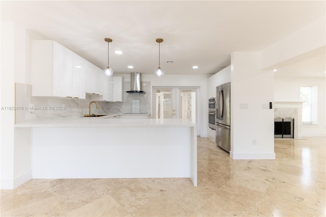 kitchen featuring wall chimney exhaust hood, stainless steel fridge, light countertops, a peninsula, and white cabinetry