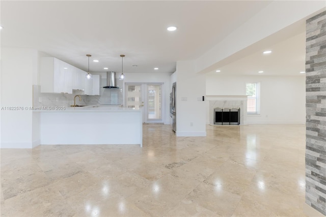 kitchen featuring white cabinets, light countertops, wall chimney range hood, open floor plan, and stainless steel fridge