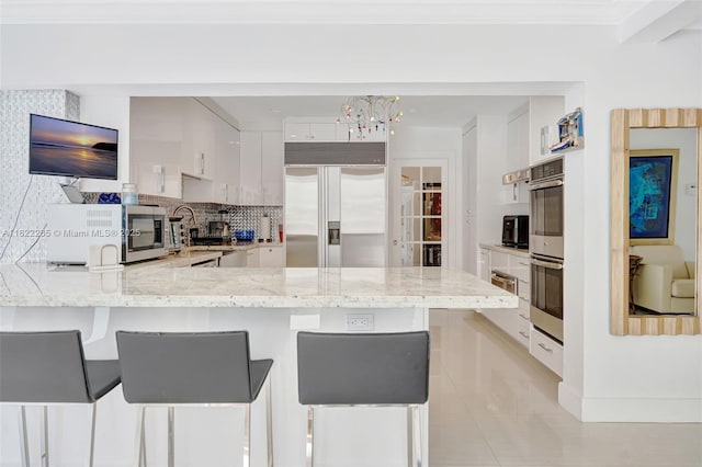 11230 SW 69th Ct, Pinecrest, FL 33156 - kitchen featuring appliances with stainless steel finishes, a peninsula, white cabinetry, light stone countertops, and crown molding
