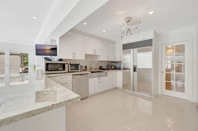 11230 SW 69th Ct, Pinecrest, FL 33156 - kitchen featuring appliances with stainless steel finishes, tasteful backsplash, light stone countertops, white cabinets, and crown molding