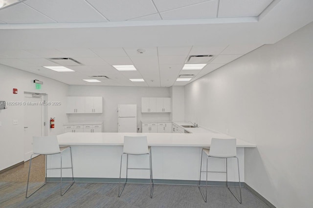 600 Three Islands Blvd Unit 615, Hallandale Beach, FL 33009 - kitchen featuring freestanding refrigerator, a peninsula, a breakfast bar area, a paneled ceiling, and white cabinets