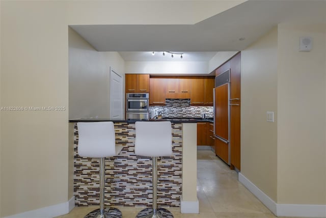 3101 S Ocean Dr Unit 404, Hollywood, FL 33019 - kitchen with brown cabinetry, dark countertops, decorative backsplash, paneled built in refrigerator, and light tile patterned flooring