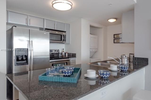 1861 NW S River Dr Unit 807, Miami, FL 33125 - kitchen with stainless steel appliances, stacked washer / dryer, a peninsula, and dark stone countertops
