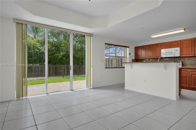 3086 SW 153rd Path, Miami, FL 33185 - kitchen featuring white microwave, light tile patterned flooring, a kitchen bar, and tasteful backsplash