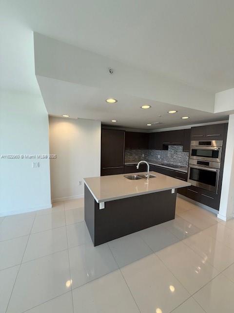 7875 NW 107th Ave Unit 410, Doral, FL 33178 - kitchen with modern cabinets, decorative backsplash, light countertops, recessed lighting, and a center island with sink