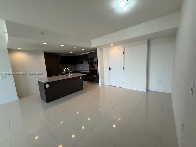 7875 NW 107th Ave Unit 410, Doral, FL 33178 - kitchen featuring tasteful backsplash, a center island with sink, light tile patterned floors, light countertops, and multiple ovens