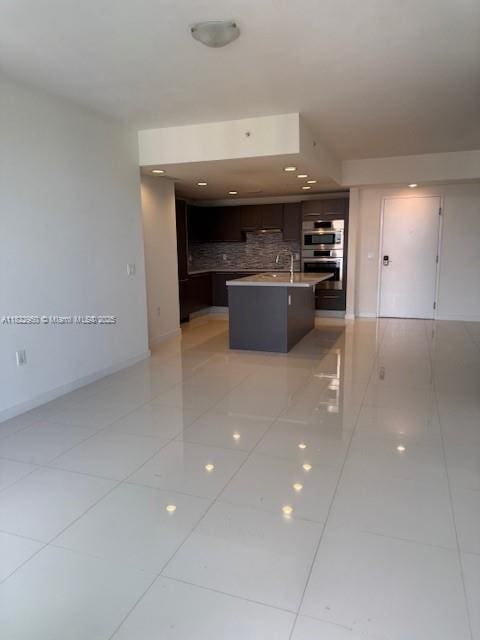7875 NW 107th Ave Unit 410, Doral, FL 33178 - kitchen featuring stainless steel double oven, light tile patterned floors, dark brown cabinets, backsplash, and an island with sink