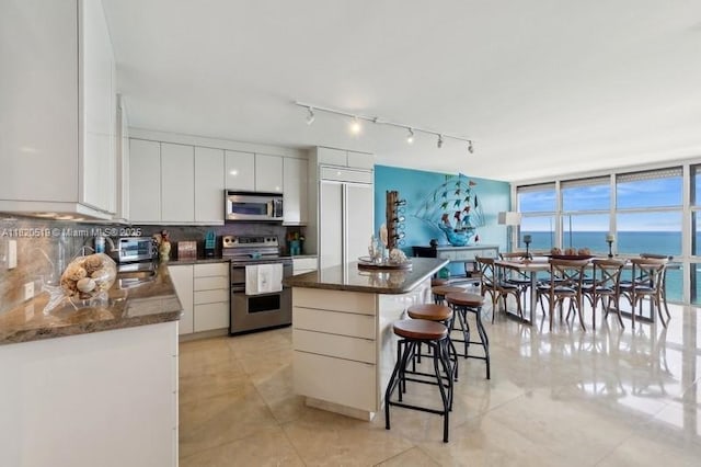 6423 Collins Ave Unit 1605, Miami Beach, FL 33141 - kitchen with appliances with stainless steel finishes, a kitchen bar, backsplash, a center island, and white cabinetry
