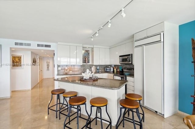 6423 Collins Ave Unit 1605, Miami Beach, FL 33141 - kitchen featuring stainless steel appliances, a breakfast bar area, tasteful backsplash, white cabinets, and a kitchen island