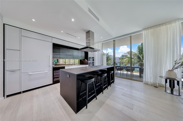 300 Collins Ave Unit 3D, Miami Beach, FL 33139 - kitchen featuring island range hood, modern cabinets, expansive windows, light wood-style flooring, and a kitchen bar
