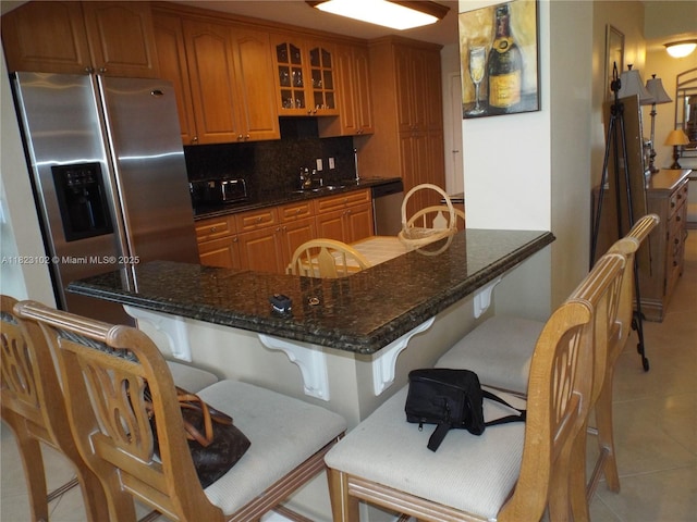 1890 S Ocean Dr Unit 504, Hallandale Beach, FL 33009 - kitchen with light tile patterned flooring, glass insert cabinets, decorative backsplash, a kitchen bar, and stainless steel appliances
