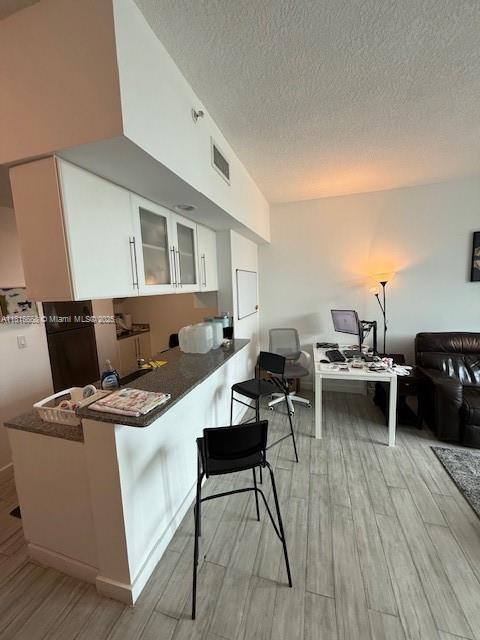 275 NE 18th St Unit 402, Miami, FL 33132 - kitchen featuring light wood finished floors, white cabinetry, glass insert cabinets, a desk, and a textured ceiling
