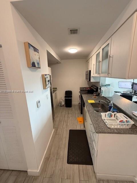 275 NE 18th St Unit 402, Miami, FL 33132 - kitchen with stainless steel appliances, light wood finished floors, white cabinetry, dark countertops, and glass insert cabinets