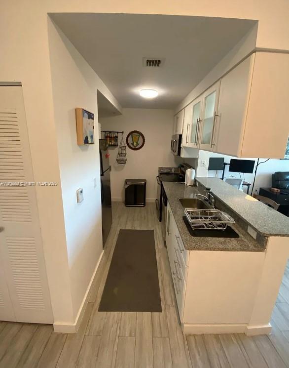 275 NE 18th St Unit 402, Miami, FL 33132 - kitchen with electric range, light wood finished floors, white cabinetry, and stainless steel microwave