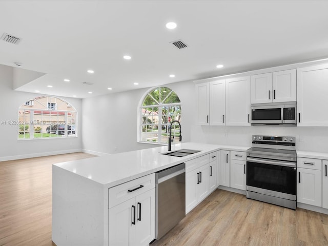 457 NW 87th Ln, Coral Springs, FL 33071 - kitchen with appliances with stainless steel finishes, light wood-type flooring, a peninsula, light countertops, and white cabinetry
