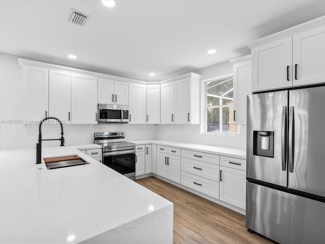 457 NW 87th Ln, Coral Springs, FL 33071 - kitchen with appliances with stainless steel finishes, white cabinetry, light wood-style floors, recessed lighting, and light stone countertops