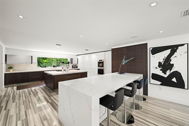 1833 W 24th St, Miami Beach, FL 33140 - kitchen featuring a center island, double oven, light wood-style floors, recessed lighting, and dark brown cabinets