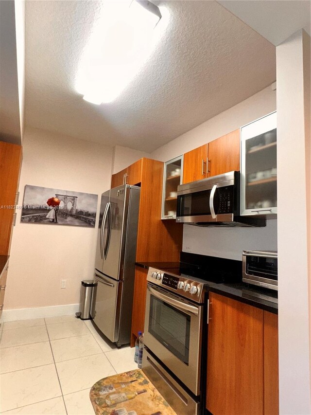 18800 NE 29th Ave Unit 412, Aventura, FL 33180 - kitchen with stainless steel appliances, brown cabinetry, dark countertops, light tile patterned flooring, and glass insert cabinets