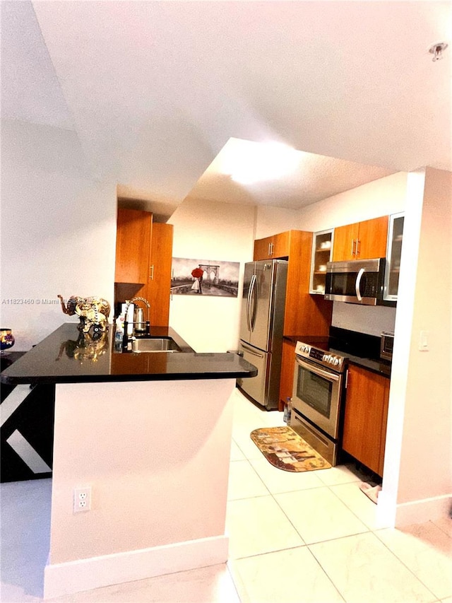18800 NE 29th Ave Unit 412, Aventura, FL 33180 - kitchen with appliances with stainless steel finishes, dark countertops, a peninsula, brown cabinetry, and glass insert cabinets