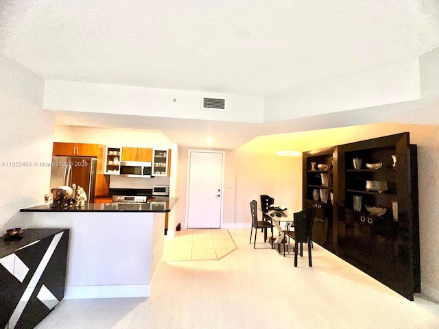 18800 NE 29th Ave Unit 412, Aventura, FL 33180 - kitchen with stainless steel appliances, dark countertops, brown cabinetry, a peninsula, and glass insert cabinets