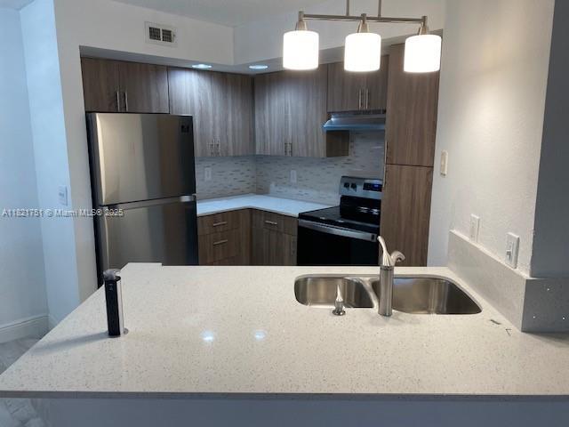 12950 Vista Isles Dr Unit 414, Sunrise, FL 33325 - kitchen with range with electric stovetop, freestanding refrigerator, under cabinet range hood, tasteful backsplash, and light stone counters