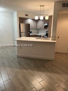 12950 Vista Isles Dr Unit 414, Sunrise, FL 33325 - kitchen featuring freestanding refrigerator, dark wood-style floors, light countertops, under cabinet range hood, and hanging light fixtures