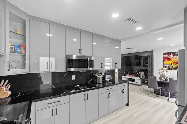 6474 Palm Ave, Hialeah, FL 33012 - kitchen with stainless steel microwave, black electric stovetop, dark countertops, light wood finished floors, and backsplash
