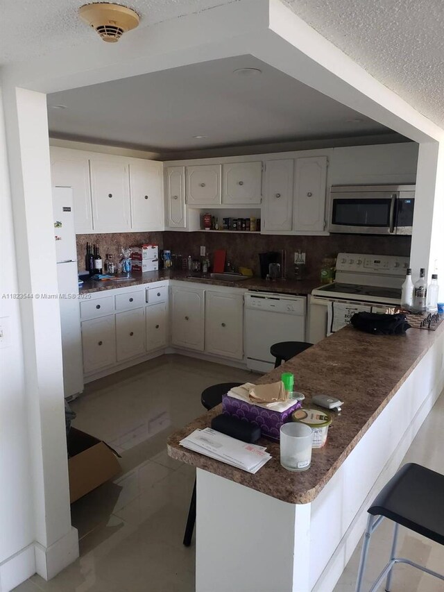 13499 Biscayne Blvd Unit 1005, North Miami, FL 33181 - kitchen featuring white appliances, white cabinets, tasteful backsplash, a peninsula, and a textured ceiling