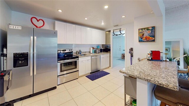 11111 Biscayne Blvd Unit 2G, Miami, FL 33181 - kitchen with appliances with stainless steel finishes, white cabinets, light tile patterned flooring, a breakfast bar, and recessed lighting