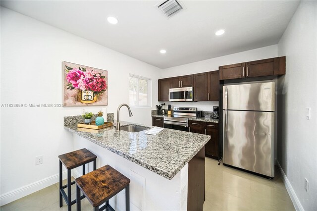 1250 NE 110th St, Miami, FL 33161 - kitchen with appliances with stainless steel finishes, dark brown cabinetry, a breakfast bar area, a peninsula, and light stone counters