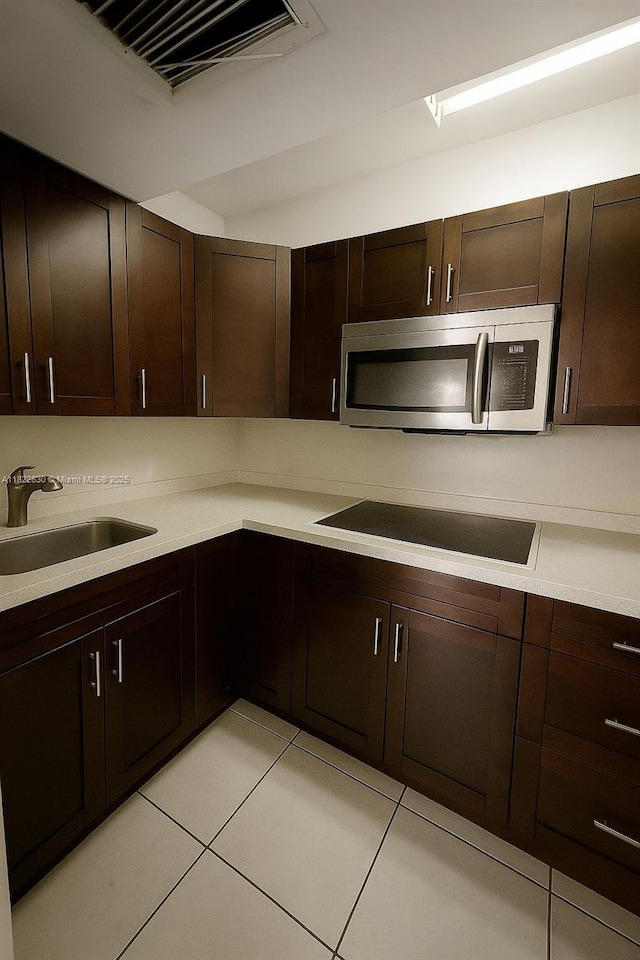 5348 W 14th Ave, Hialeah, FL 33012 - kitchen with stainless steel microwave, black electric cooktop, light countertops, light tile patterned floors, and dark brown cabinetry