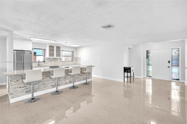 2035 SW 15th Ct, Deerfield Beach, FL 33442 - kitchen with stainless steel refrigerator, a breakfast bar area, decorative backsplash, white cabinetry, and glass insert cabinets