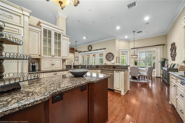 3859 Enchanted Oaks Ln, Sebring, FL 33875 - kitchen featuring a peninsula, stainless steel dishwasher, cream cabinetry, glass insert cabinets, and dark stone countertops