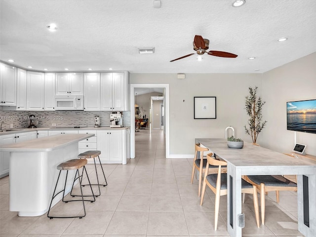 3920 NW 20th St, Coconut Creek, FL 33066 - kitchen featuring white microwave, light countertops, tasteful backsplash, ceiling fan, and white cabinets