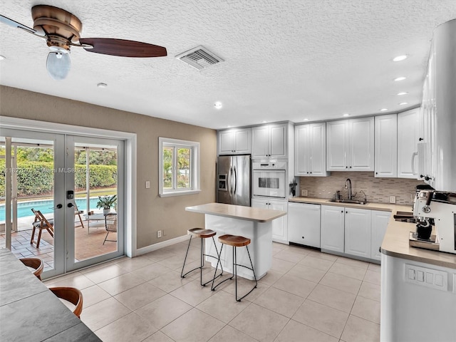 3920 NW 20th St, Coconut Creek, FL 33066 - kitchen with white appliances, french doors, light tile patterned floors, a breakfast bar, and recessed lighting