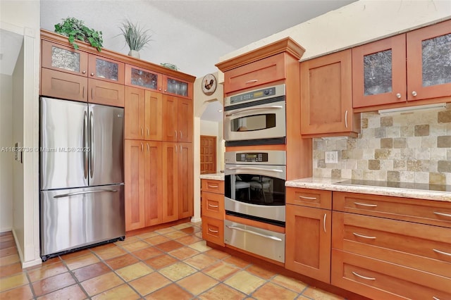 1180 NW 100th Way, Plantation, FL 33322 - kitchen with stainless steel appliances, a warming drawer, tasteful backsplash, brown cabinetry, and glass insert cabinets