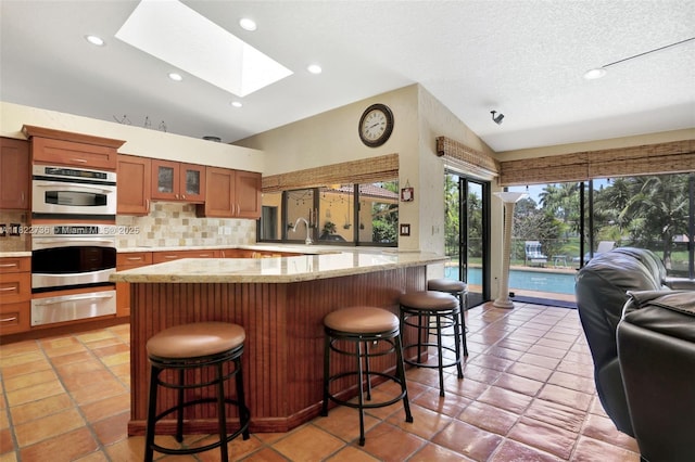 1180 NW 100th Way, Plantation, FL 33322 - kitchen with a warming drawer, a skylight, tasteful backsplash, brown cabinetry, and glass insert cabinets