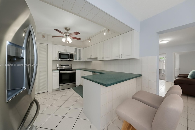 359 E 19th St, Hialeah, FL 33010 - kitchen with stainless steel appliances, dark countertops, a peninsula, light tile patterned floors, and white cabinetry