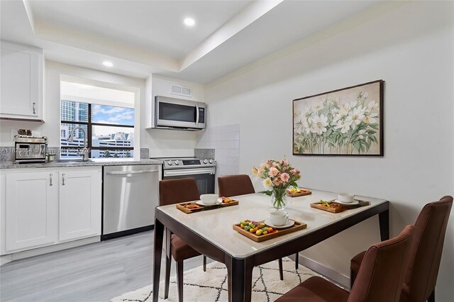 600 Parkview Dr Unit 624, Hallandale Beach, FL 33009 - kitchen featuring stainless steel appliances, light wood-style flooring, white cabinetry, a tray ceiling, and light stone counters