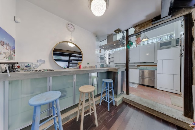 305 Jefferson Ave Unit 5, Miami Beach, FL 33139 - kitchen featuring wall chimney exhaust hood, stainless steel microwave, a kitchen bar, and wood finished floors