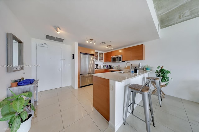 3250 NE 1st Ave Unit 1007, Miami, FL 33137 - kitchen with appliances with stainless steel finishes, a peninsula, brown cabinetry, a kitchen bar, and light countertops