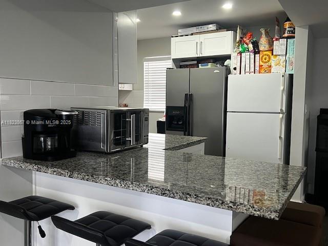 14165 SW 87th St Unit D202, Miami, FL 33183 - kitchen with stainless steel fridge, freestanding refrigerator, dark stone counters, white cabinetry, and recessed lighting