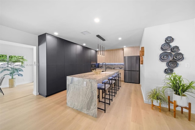 11530 NE 7th Ave, Biscayne Park, FL 33161 - kitchen with freestanding refrigerator, modern cabinets, light wood-style flooring, a breakfast bar area, and a center island with sink